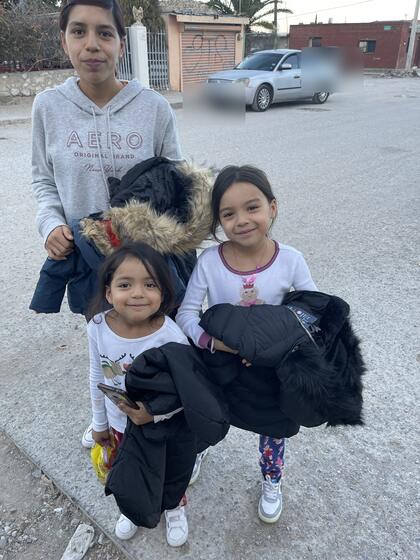 A woman and two young girls on a street holding new winter coats.